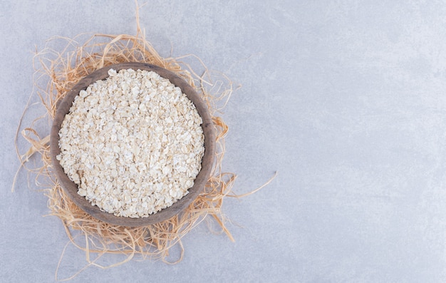 Wooden bowl placed on a pile of straw and filled with oat on marble surface