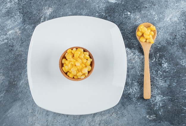 A wooden bowl of popcorn seeds onn empty plate .