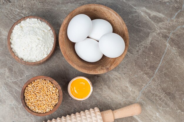 Wooden bowl of raw eggs, flour and barley on marble surface.