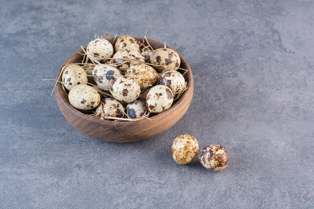 Wooden bowl of raw quail eggs on stone table.