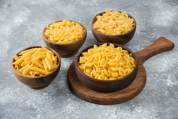 Wooden bowl of raw various pasta on marble.