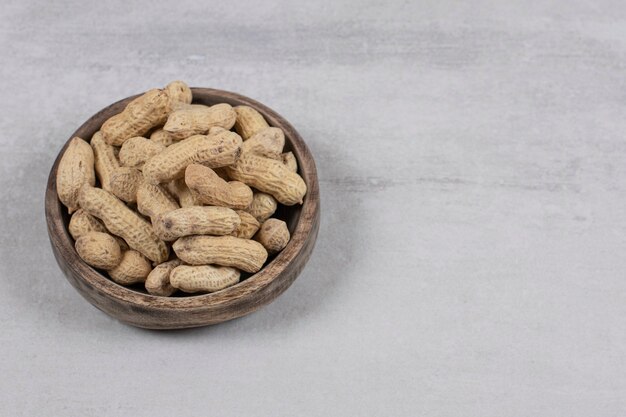 Wooden bowl of shelled peanuts on marble background.