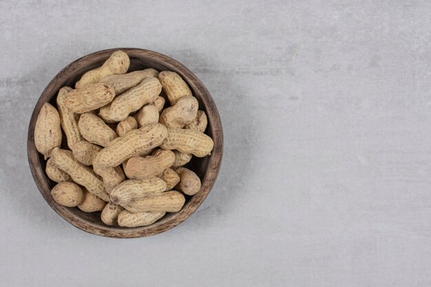 Wooden bowl of shelled peanuts on marble background.