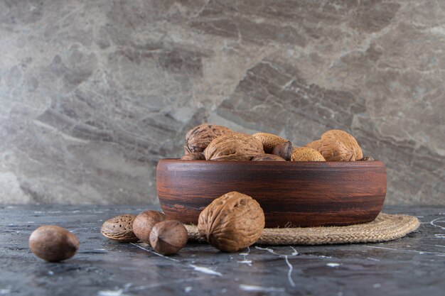 Wooden bowl of shelled various nuts on marble surface. 