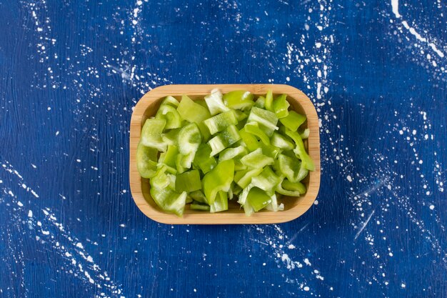 Free photo wooden bowl of sliced green bell peppers on marble surface.