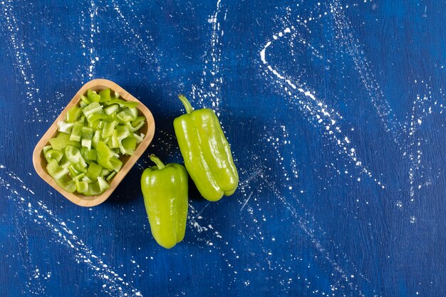 Wooden bowl of sliced green bell peppers and whole peppers