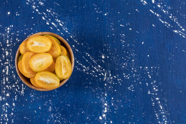 Wooden bowl of sliced kumquat fruits on marble surface. 