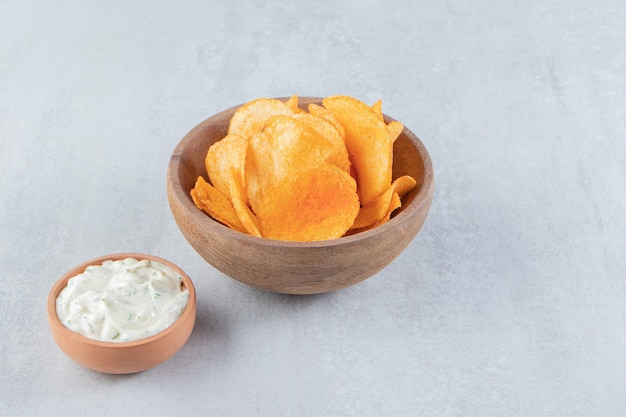 Wooden bowl of spicy chips and sauce on stone.