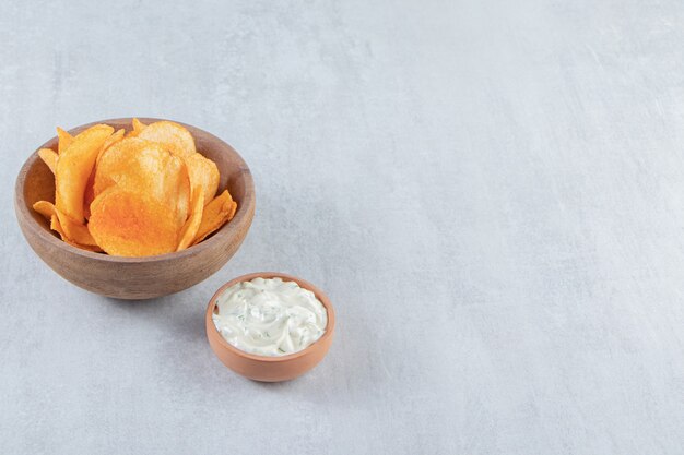 Wooden bowl of spicy chips and sauce on stone.