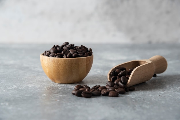 Wooden bowl and spoon of roasted coffee beans on marble.