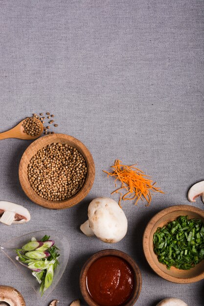 Wooden bowl of spring onion; coriander seeds; sauce; mushroom and grated carrot on grey linen tablecloth