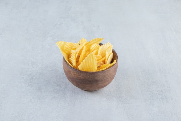 Wooden bowl of tasty ripple chips on stone.