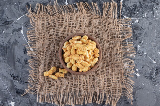 Wooden bowl of tasty salted crackers on marble table. 