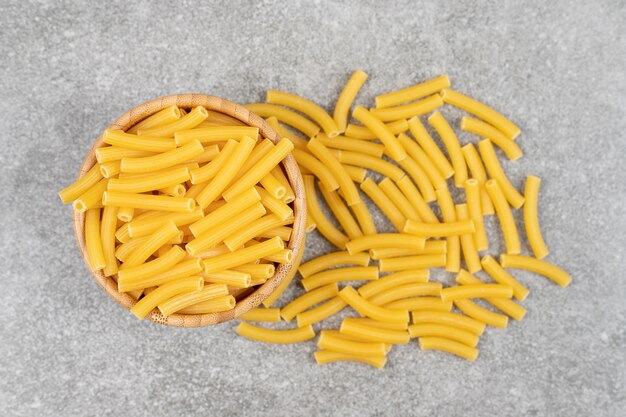 Wooden bowl of uncooked macaroni on marble surface