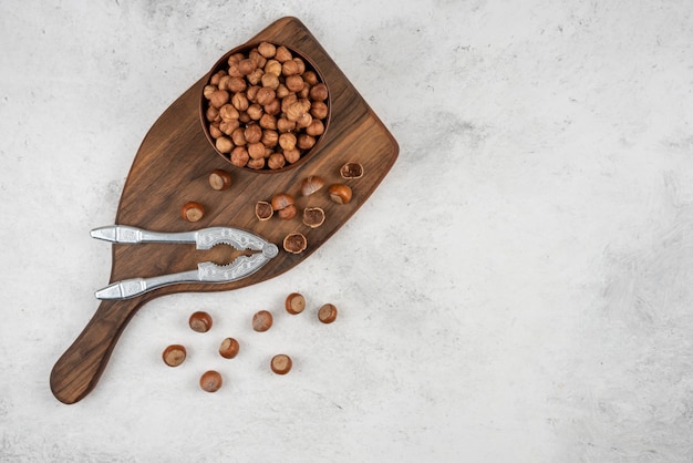 Wooden bowl of unpeeled organic hazelnut kernels on cutting board. 