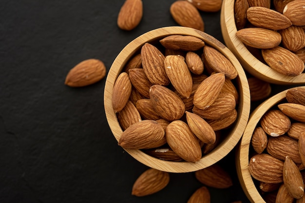 Wooden bowl with almond on black background. Top view.