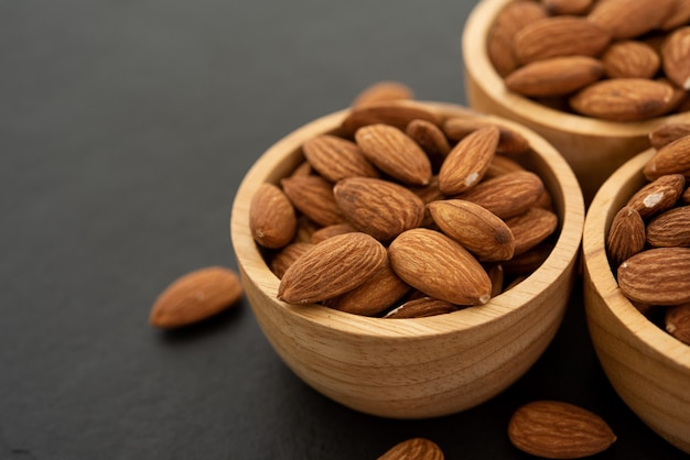 Wooden bowl with almond on black background. Top view.