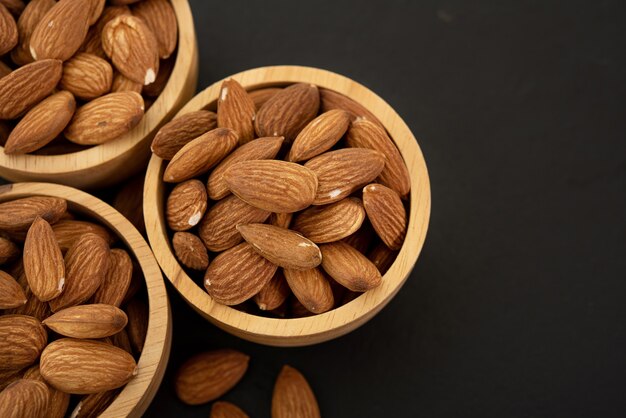 Wooden bowl with almond on black background. Top view.