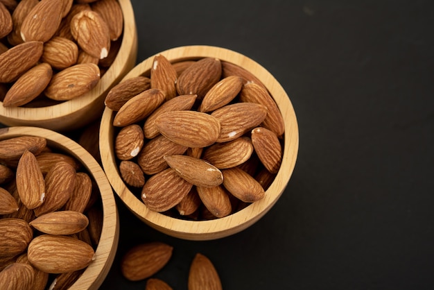 Wooden bowl with almond on black background. Top view.