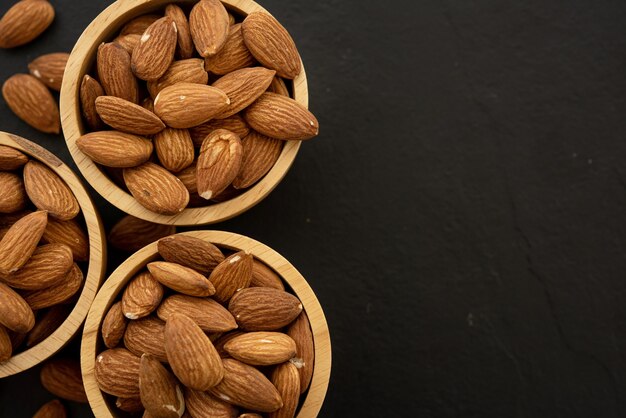 Wooden bowl with almond on black background. Top view.