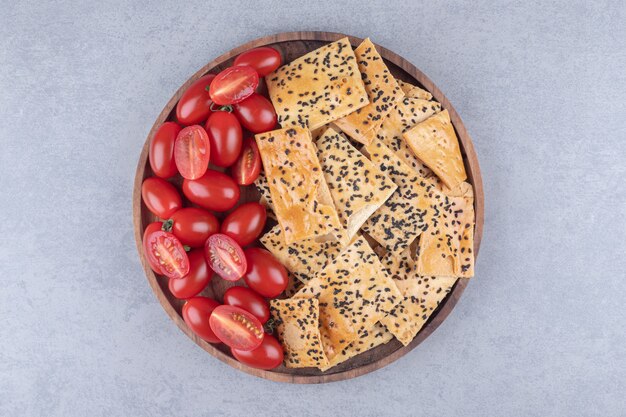 wooden bowl with crispy crackers and tomatoes on stone surface