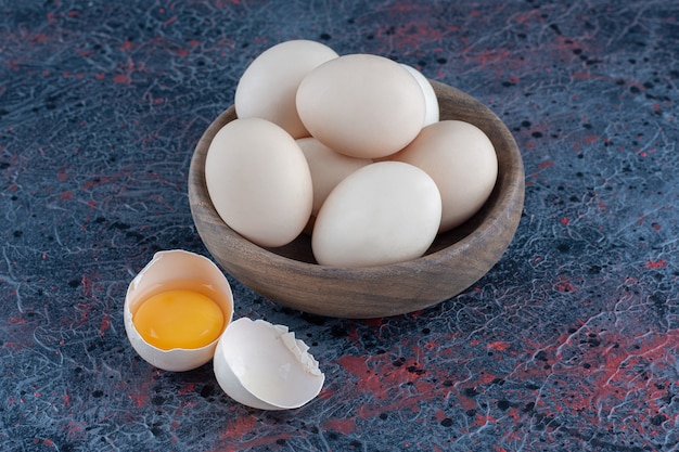 A wooden bowl with fresh raw chicken eggs .