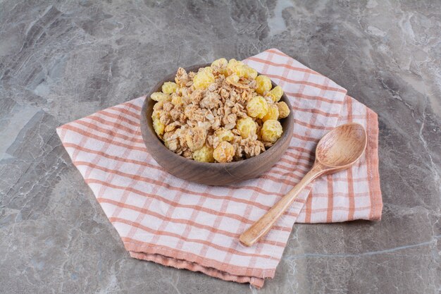 A wooden bowl with healthy cornflakes and an empty wooden spoon . 