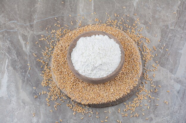 A wooden bowl with oat grains on marble surface