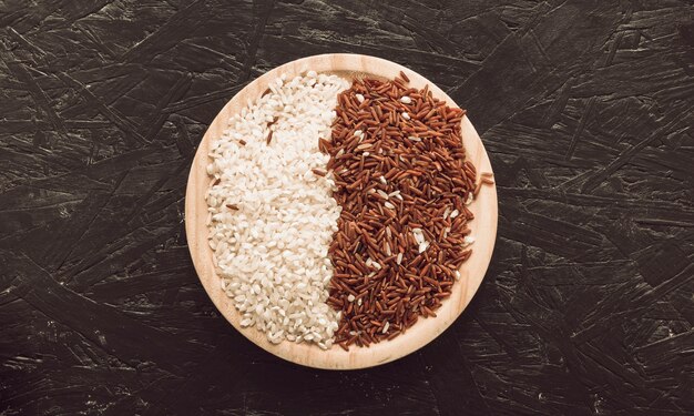 Wooden bowl with raw red long grain jasmine and white rice on rough background