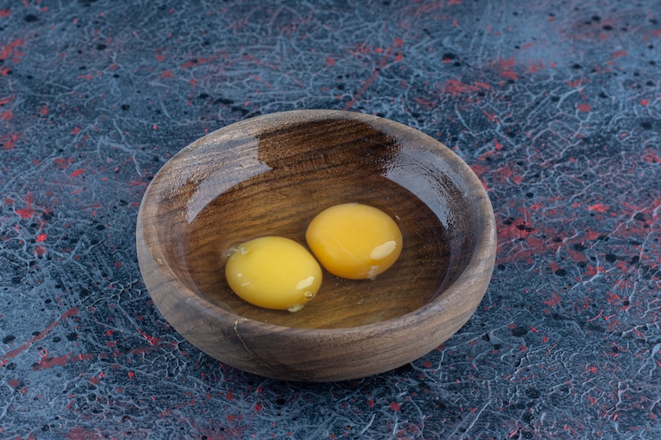 Free Photo a wooden bowl with two raw chicken eggs .