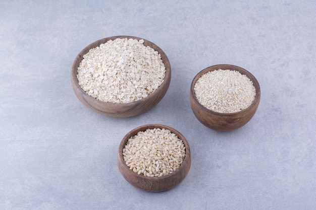 Wooden bowls filled with rice, oat and oat flakes on marble surface