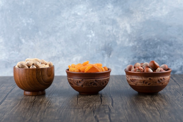 Wooden bowls full of healthy nuts with dried apricot fruits on wooden table .