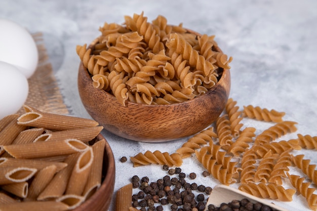 Foto gratuita ciotole di legno di pasta secca cruda italiana con grani di pepe. foto di alta qualità