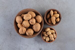 wooden bowls of organic shelled walnuts, almonds and peanuts on stone surface