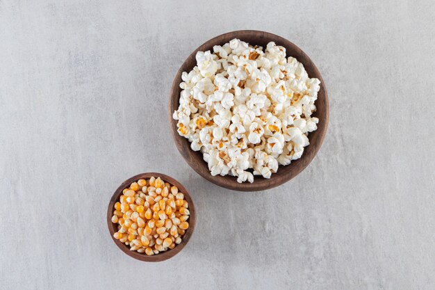 Wooden bowls of popcorn and raw corn kernels on stone background. 