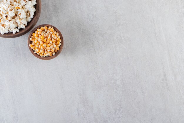 Деревянные миски попкорна и сырых кукурузных зерен на каменном столе.