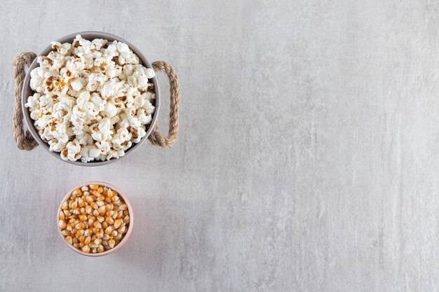 Wooden bowls of popcorn and raw corn kernels on stone table.