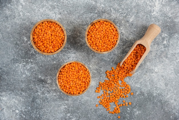 Wooden bowls of red raw lentils on marble table.