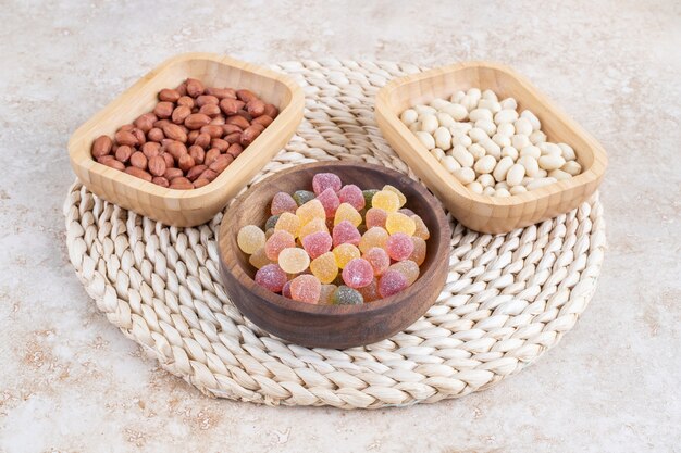 Wooden bowls of sweet candies and peanut kernels on marble surface. 