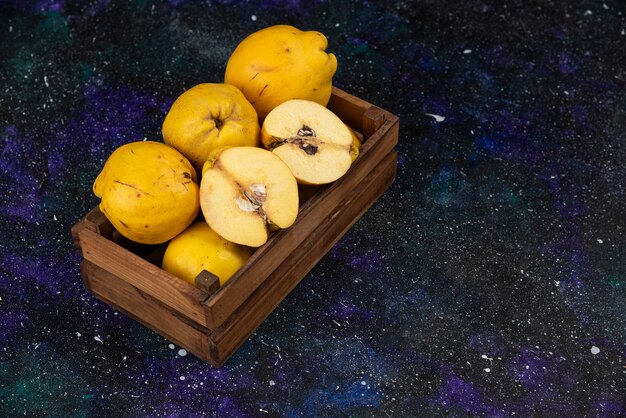 Wooden box of fresh ripe quinces on dark table. 