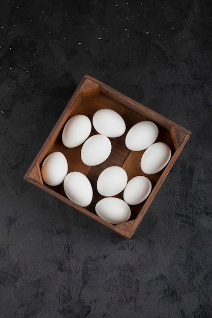 Wooden box full of organic raw eggs on black surface.