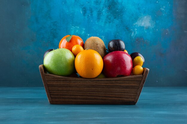 Wooden box full of various organic fruits on blue surface.