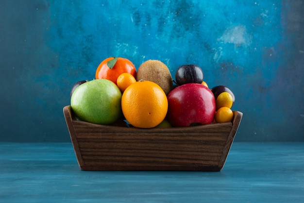 Деревянная коробка, полная различных органических фруктов на синей поверхности.