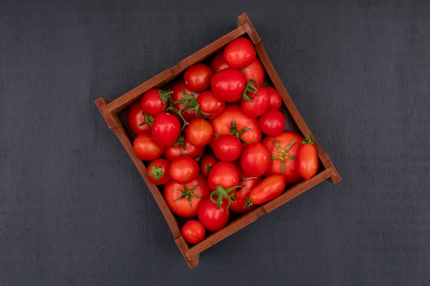黒い表面の上面に赤の明るい新鮮なトマトでいっぱい木箱