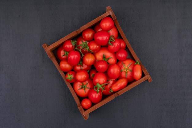 검은 표면 위에 빨간 밝은 신선한 토마토 가득한 나무 상자