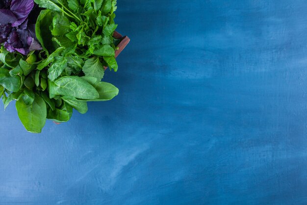 Wooden box of healthy greens placed on blue table.