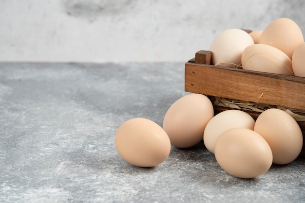 Wooden box of organic raw eggs on marble surface.
