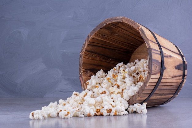 Free photo wooden bucket fallen over, spilling out popcorn on marble background. high quality photo