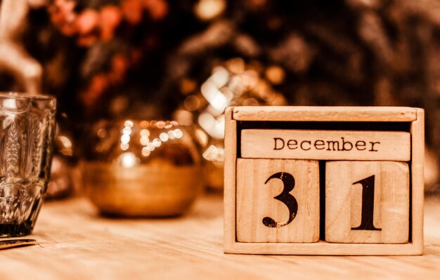お祝い​の​新年​の​装飾​を​背景​に​、​12​月​31​日​の​日付​の​木製​カレンダー​が​テーブル​の​上に​立っています​。​写真