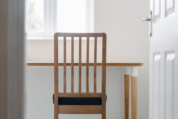 Wooden chair and a table in a white peaceful room shot through a door opening